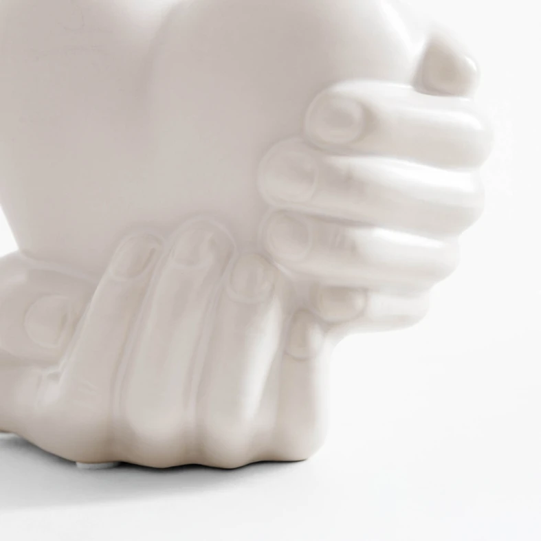 Biała dekoracja w kształcie dłoni trzymających serce.