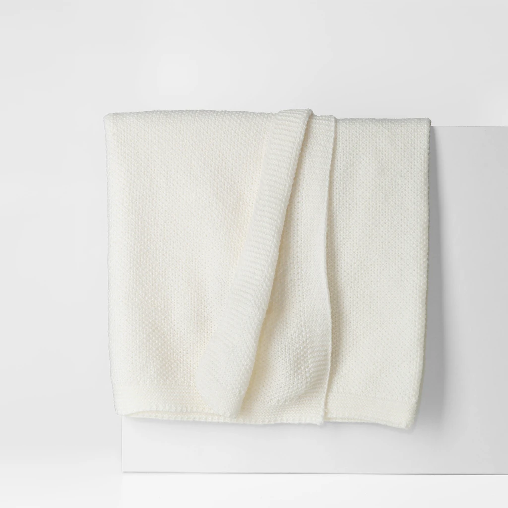 Koc w kolorze ecru, o delikatnej, dzianinowej strukturze. O prostych, estetycznie wykończonych krawędziach.