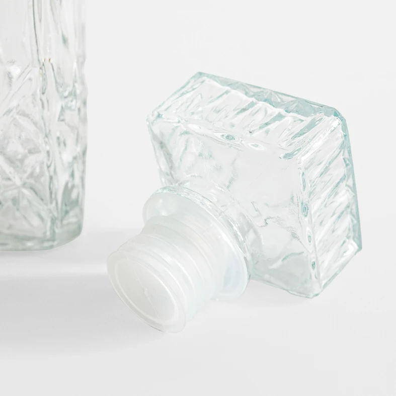 Zbliżenie na szklany korek parafki z wzorem szlifu. Ma kształt płaskiego prostopadłościanu i uszczelkę z tworzywa. 