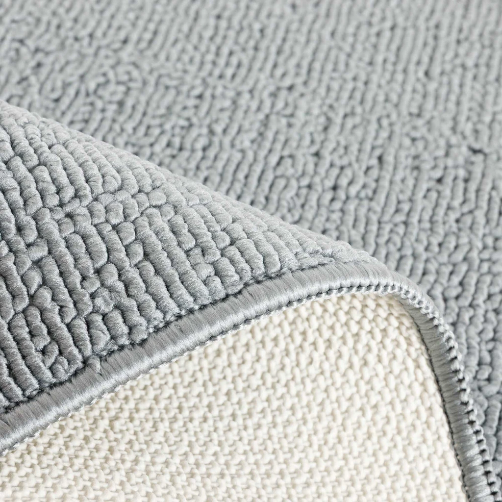 Zbliżenie na zagięty dywanik, widoczna wierzchnia, szara, poliestrowa powierzchnia i jasnobeżowy spód z lateksu.