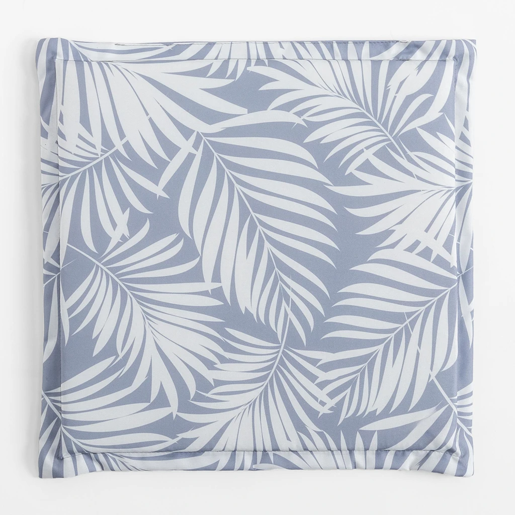 Kwadratowa, płaska poduszka ogrodowa, o wzorze białych liści palmowych na szarym tle, o gładkim, szarym tyle.