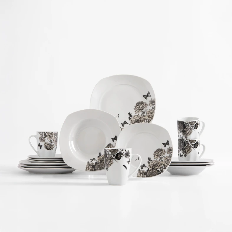 Zestaw obiadowy z delikatnym kwiatowym wzorem na białej porcelanie. Rysunek kwiatów piwonii i wirujących wokół nich motyli, uzupełniony kolorem jasnej sepii. Widoczne talerze obiadowe, głębokie i deserowe oraz kubki.