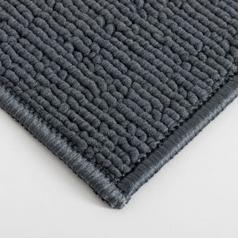 Zbliżenie na gęstą, pętelkową powierzchnię ciemnoszarego dywanika łazienkowego ze starannie obszytym brzegiem.