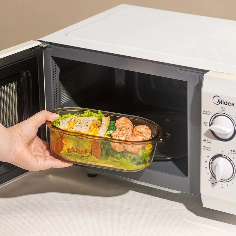 Szklany pojemnik z posiłkiem, bez wieczka, jest wkładany do mikrofali. 
