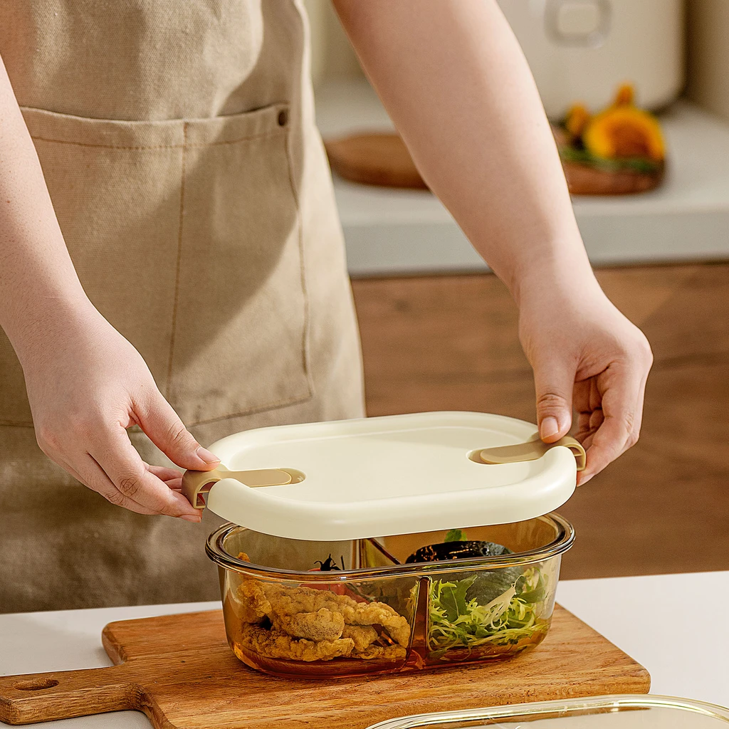 Dwie dłonie nakładają pokrywkę na owalny pojemnik z przegródką, do którego wcześniej zapakowano danie.