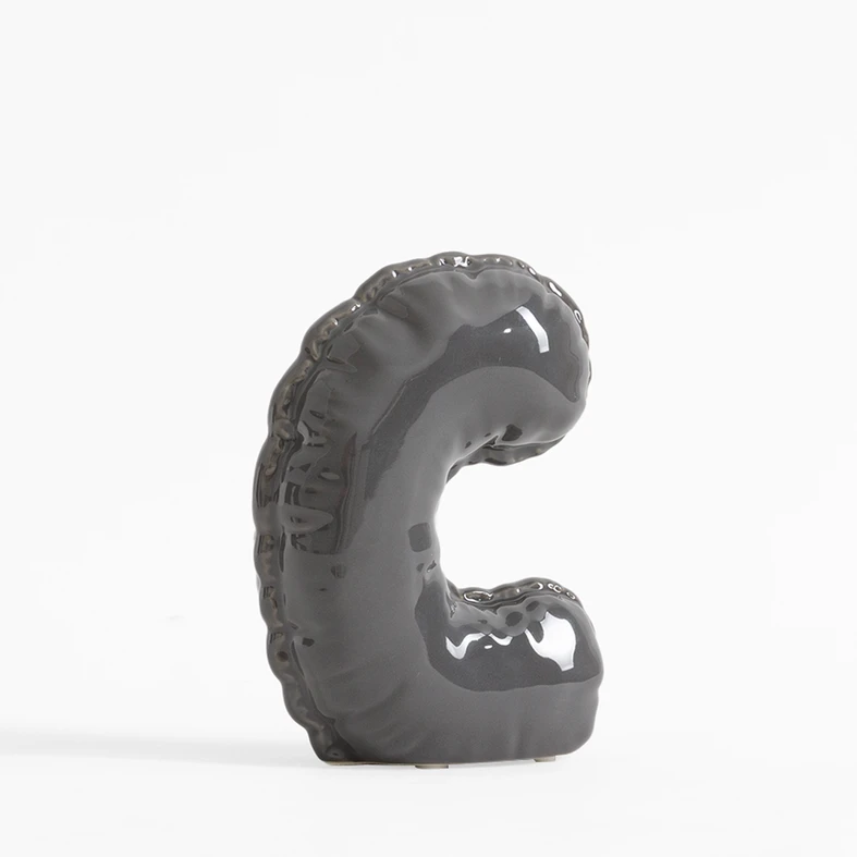 Szara figurka dekoracyjna w kształcie litery C.