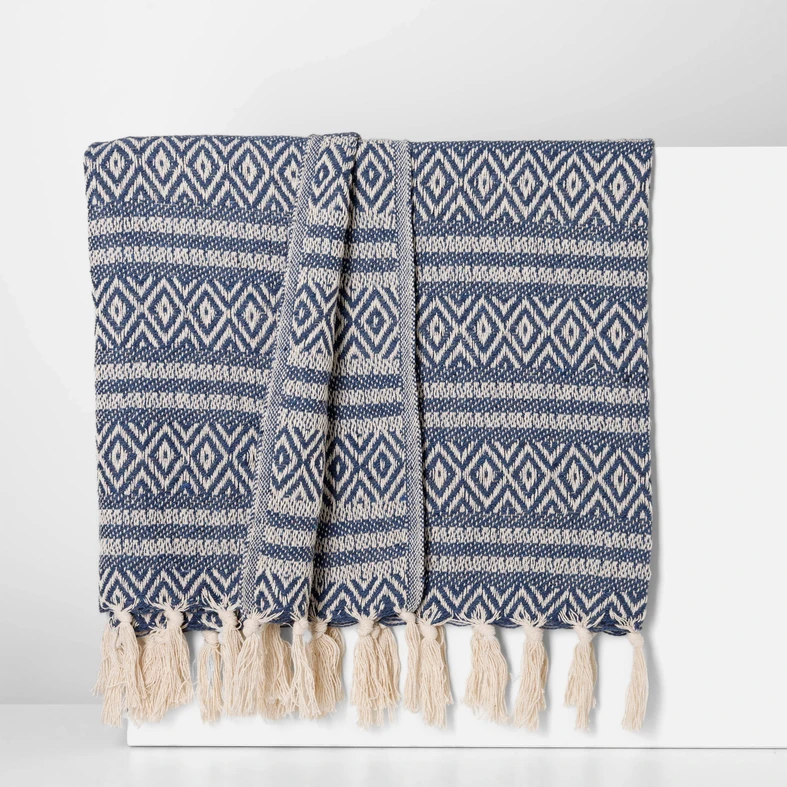 Elegancki pled o ciemnoniebiesko-kremowym splocie, zakończony kremowymi frędzlami.