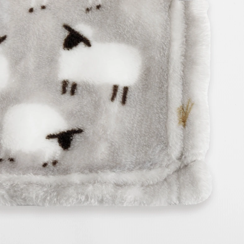 Detal, staranne wykończenie krawędzi koca z owieczkami.