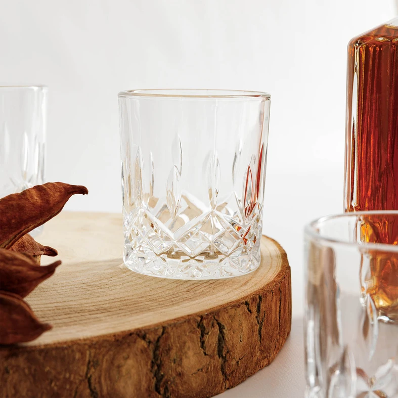 Zbliżenie na szklankę do whisky ozdobioną kryształowym szlifem, ustawioną na drewnianym krążku. 