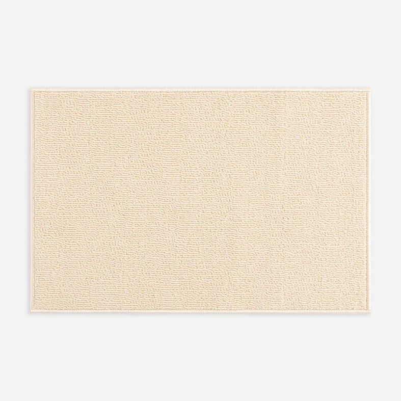 Widok z góry na beżowy dywanik łazienkowy o widocznej pętelkowej strukturze. 