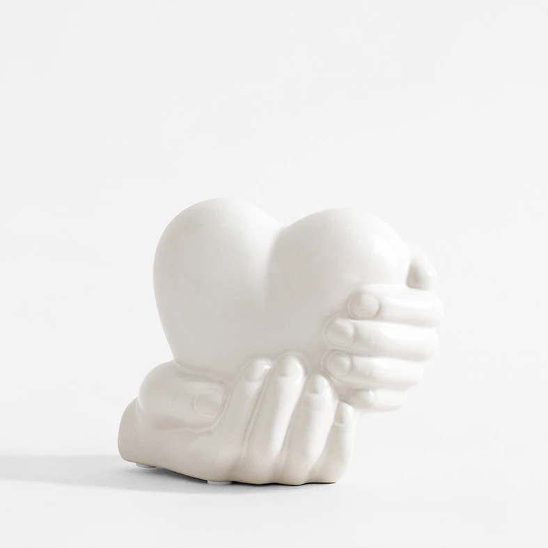 Biała dekoracja w kształcie dłoni trzymających serce.