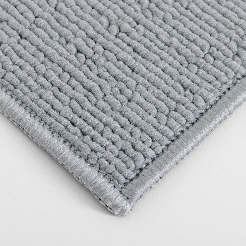 Zbliżenie na gęstą, pętelkową powierzchnię szarego dywanika łazienkowego ze starannie obszytym brzegiem.