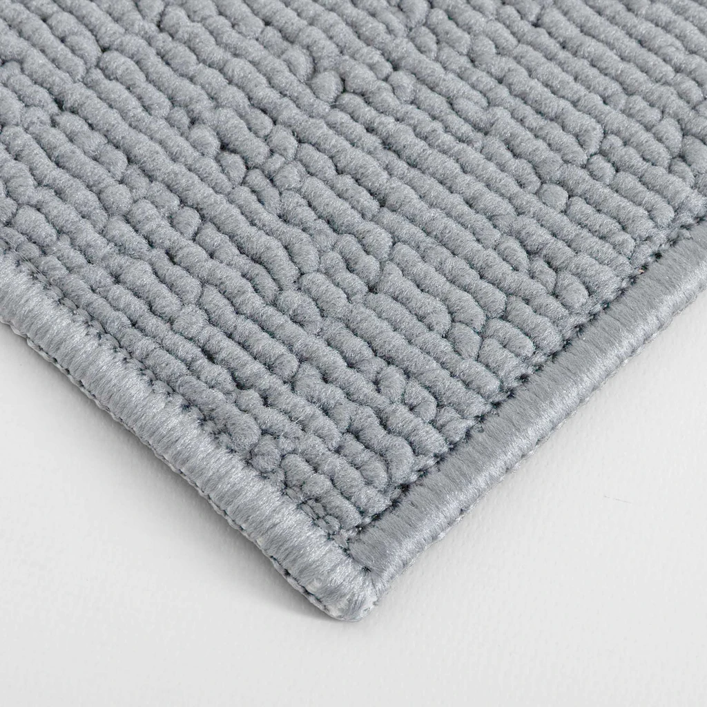 Zbliżenie na gęstą, pętelkową powierzchnię szarego dywanika łazienkowego ze starannie obszytym brzegiem.