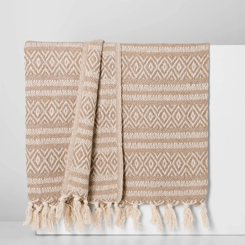 Elegancki pled o beżowo-kremowym splocie, zakończony kremowymi frędzlami.