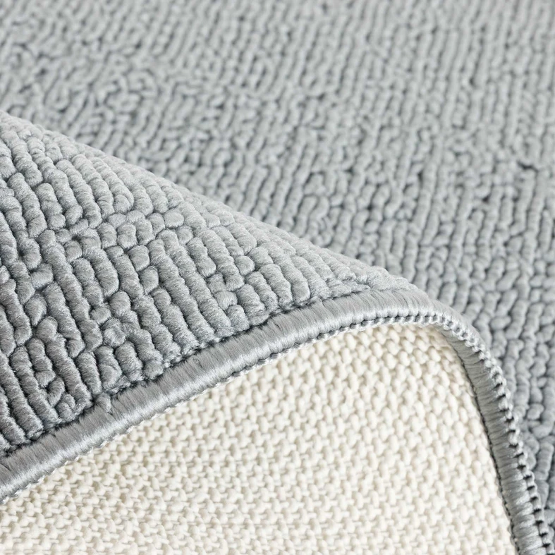 Zbliżenie na zagięty dywanik, widoczna wierzchnia, szara, poliestrowa powierzchnia i jasnobeżowy spód z lateksu.