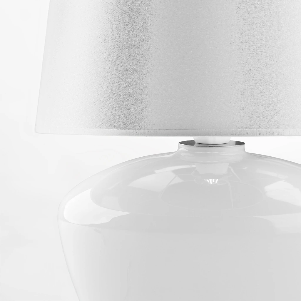 Abażur ma klasyczny kształt trapezu, opinająca go tkanina jest biała.