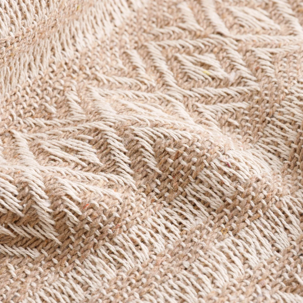 Zbliżenie na geometryczny splot pledu, łączący romby i paski.