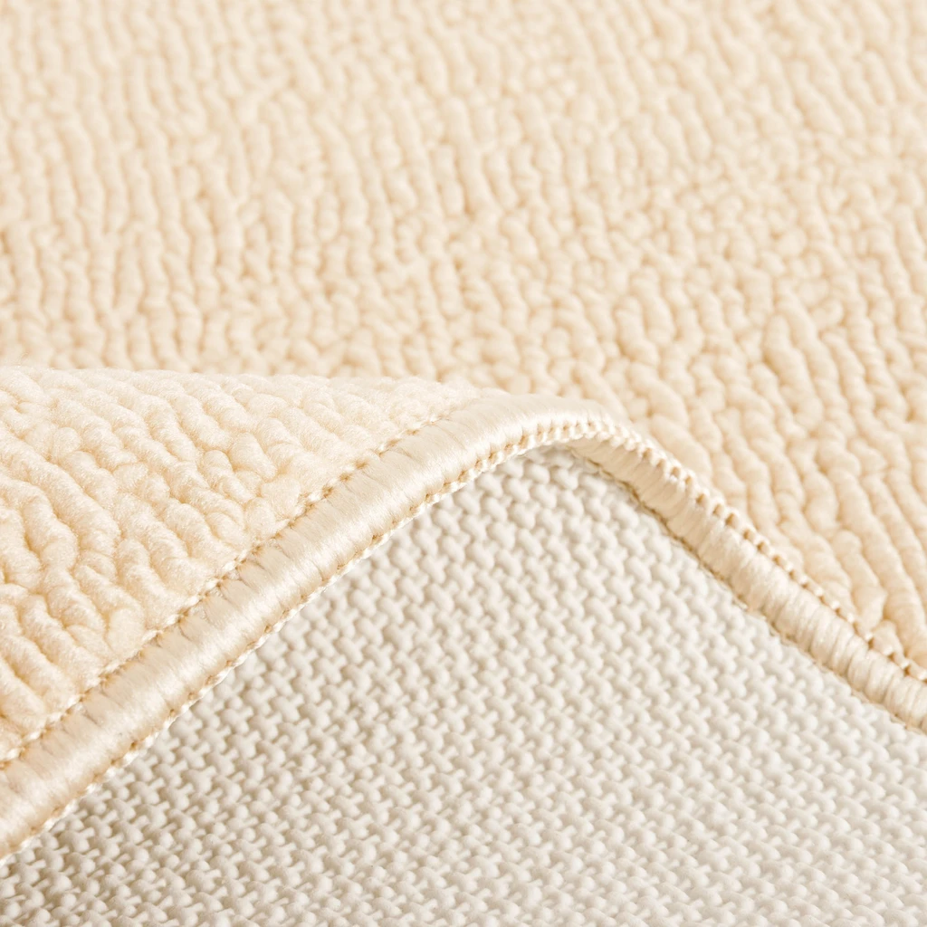 Zbliżenie na zagięty dywanik, widoczna wierzchnia, beżowa, poliestrowa powierzchnia i jasnobeżowy spód z lateksu.