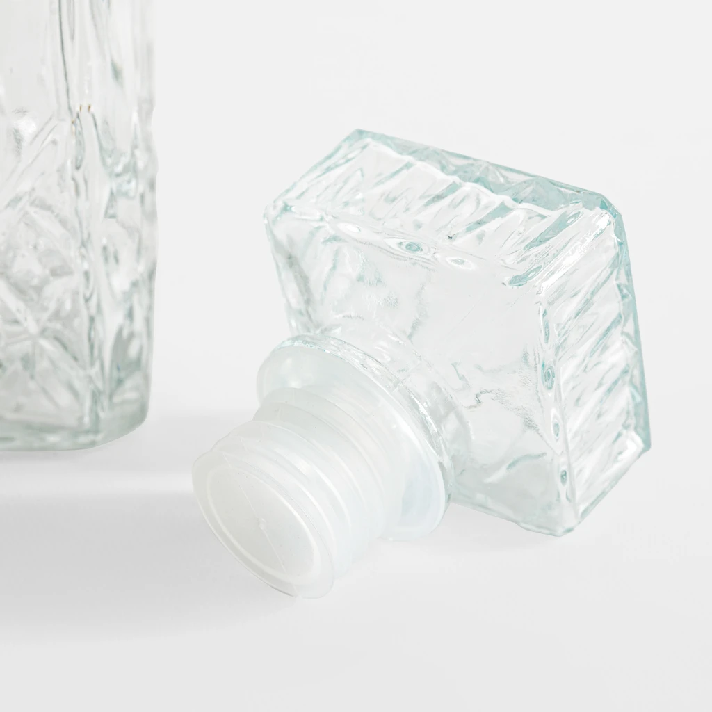 Zbliżenie na szklany korek parafki z wzorem szlifu. Ma kształt płaskiego prostopadłościanu i uszczelkę z tworzywa. 