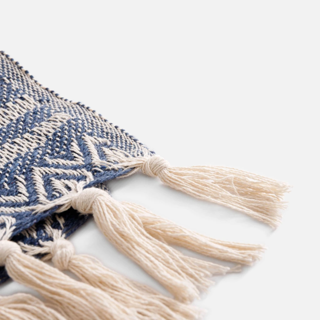 Detal, frędzle z kilku skręconych ze sobą pasm przędzy w kolorze kremowym, a następnie związane w supełki przy krawędzi pledu.