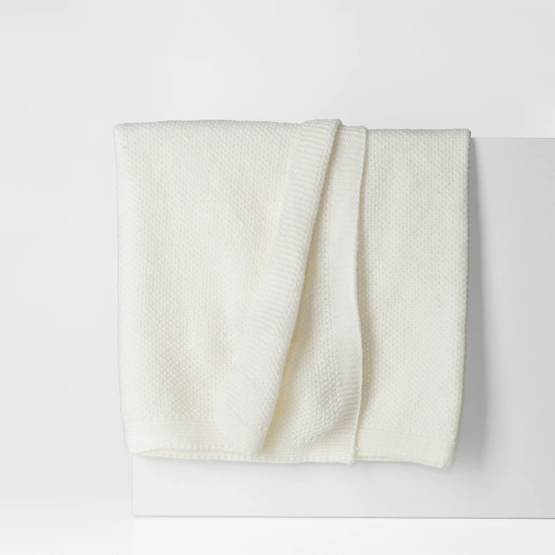 Koc w kolorze ecru, o delikatnej, dzianinowej strukturze. O prostych, estetycznie wykończonych krawędziach.