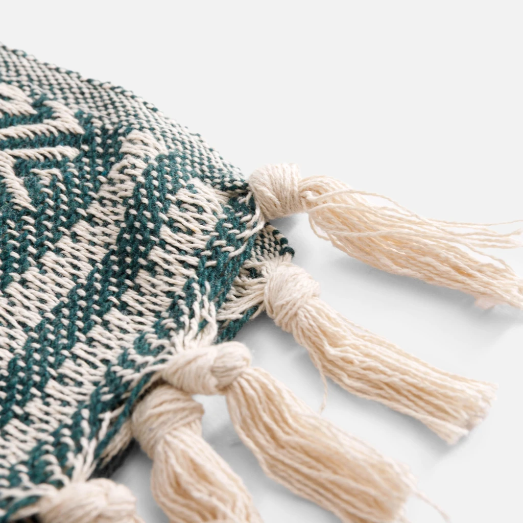 Detal, frędzle z kilku skręconych ze sobą pasm przędzy w kolorze kremowym, a następnie związane w supełki przy krawędzi pledu.