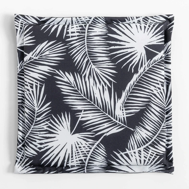 Kwadratowa, płaska poduszka ogrodowa, o wzorze białych liści palmowych na czarnym tle, o gładkim, czarnym tyle.
